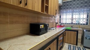A kitchen with wooden cabinets, a microwave, and a refrigerator. - One bedroom apartment East legon  (Accra)