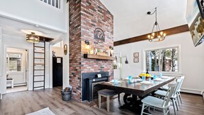 A modern kitchen with a brick fireplace, wooden dining table, and white chairs. - Stunning Lakefront Oasis—Hot Tub, Beach & Luxury! (E Wakefield)