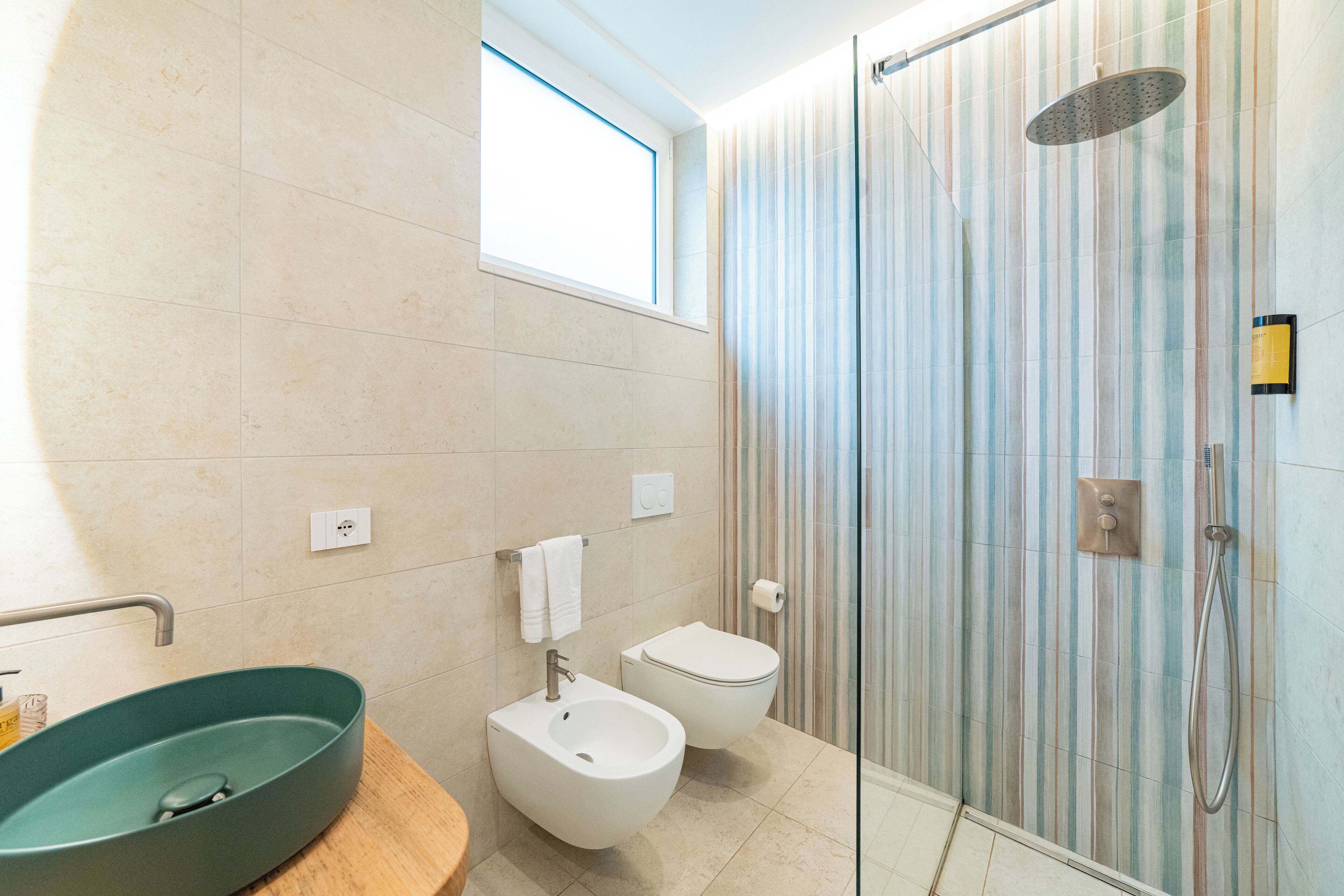 A modern bathroom with a large oval sink, a bidet, a toilet, and a glass shower enclosure.