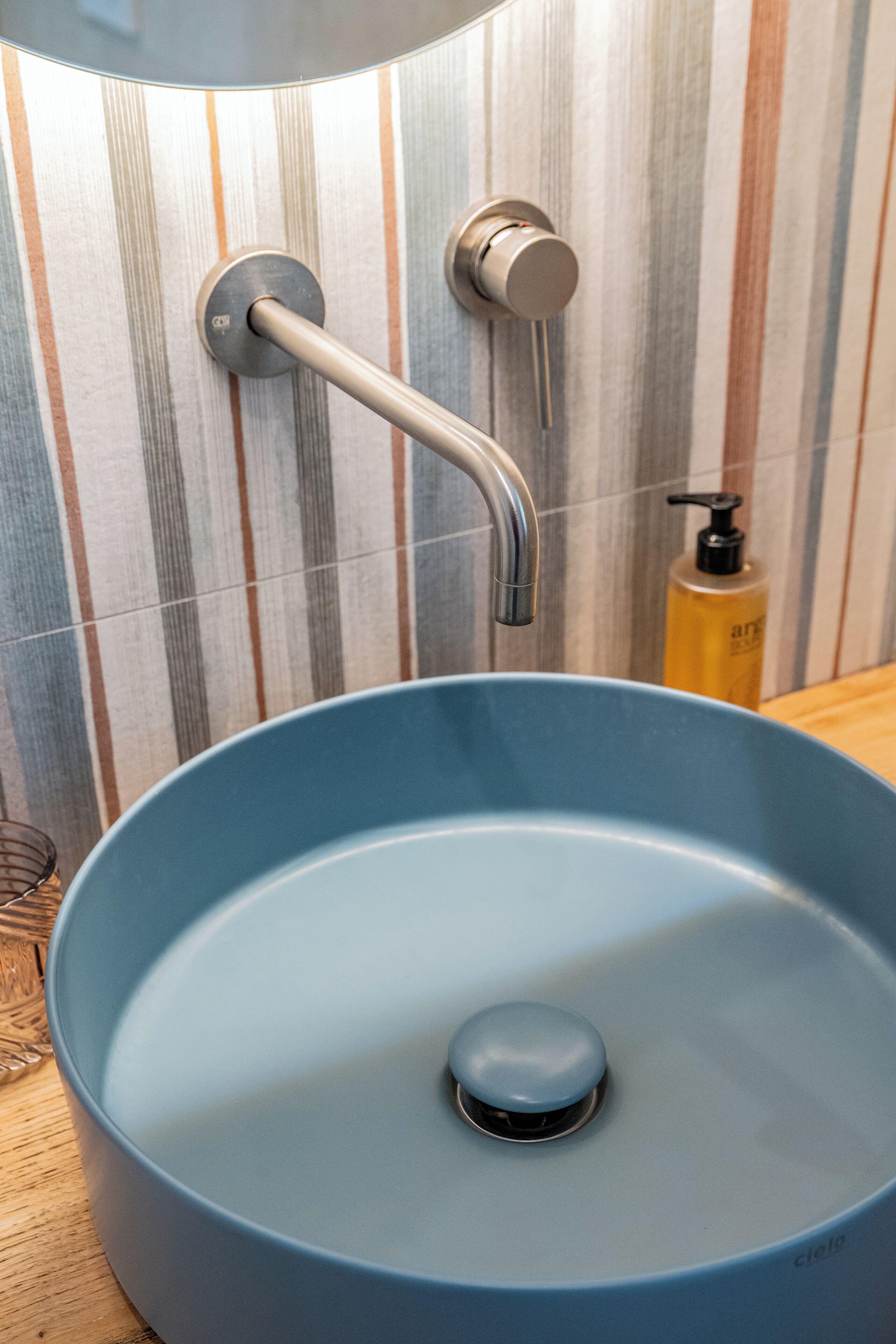Een badkamer met een blauwe wastafel, een moderne kraan en wandtegels met strepen.