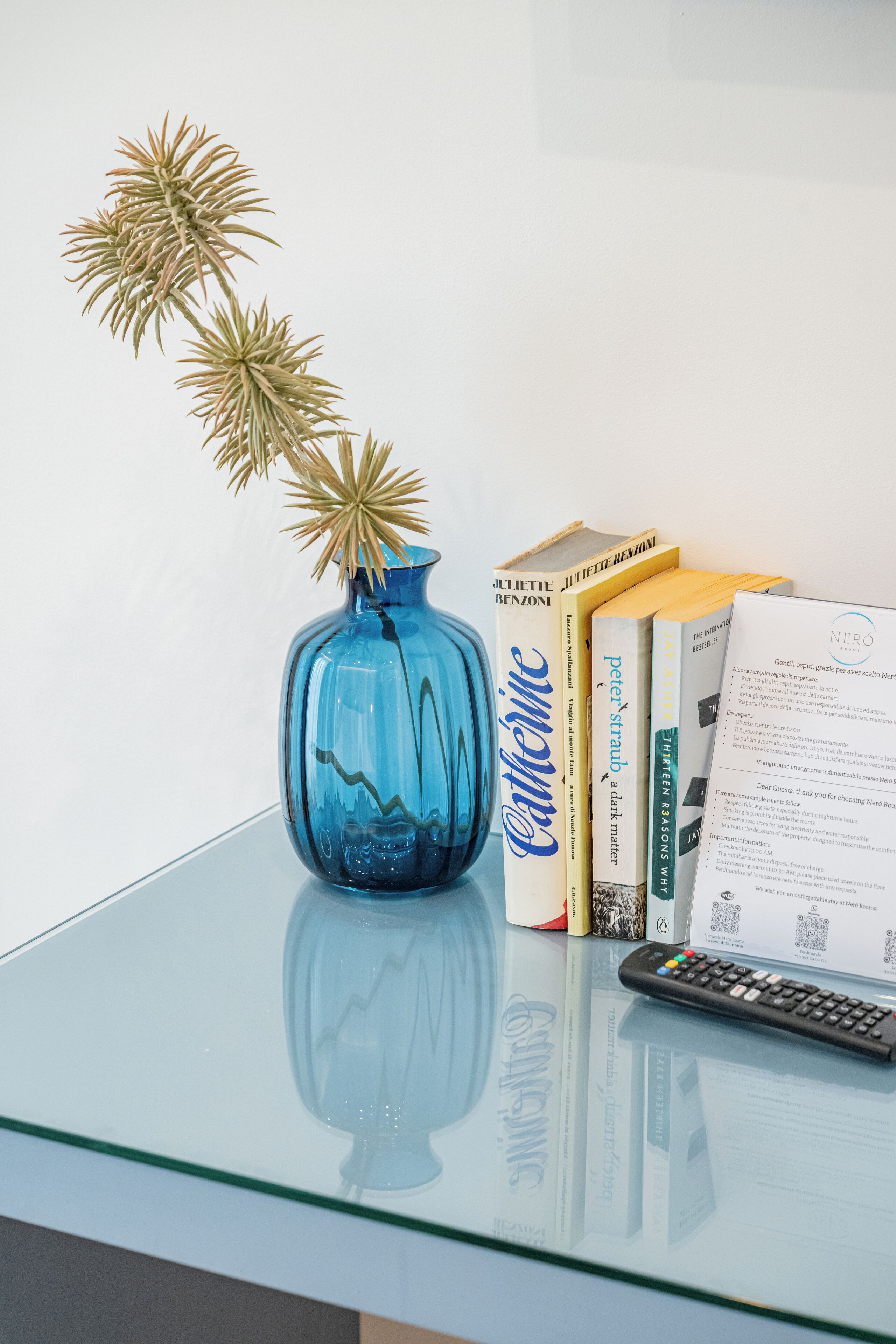 A glass table with a blue vase, books, a remote control, and a document.