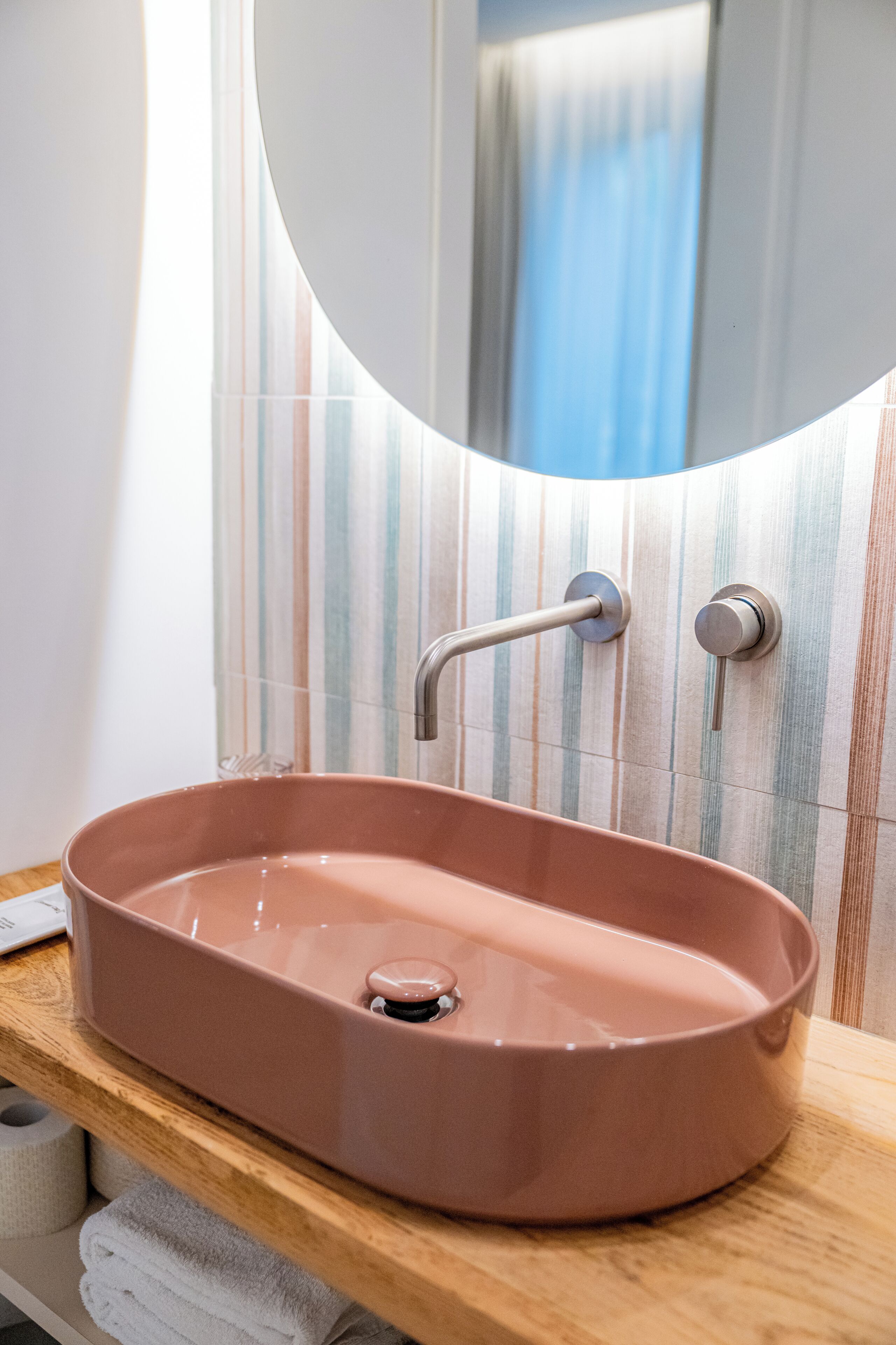 A bathroom with a pink sink, a wooden countertop, and a striped tile backsplash.
