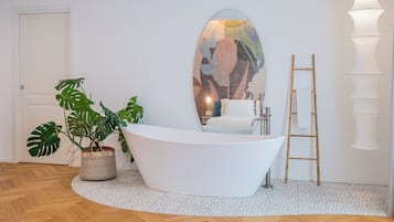 Une salle de bain moderne avec une baignoire sur pieds, un grand miroir, un lavabo et une plante en pot.