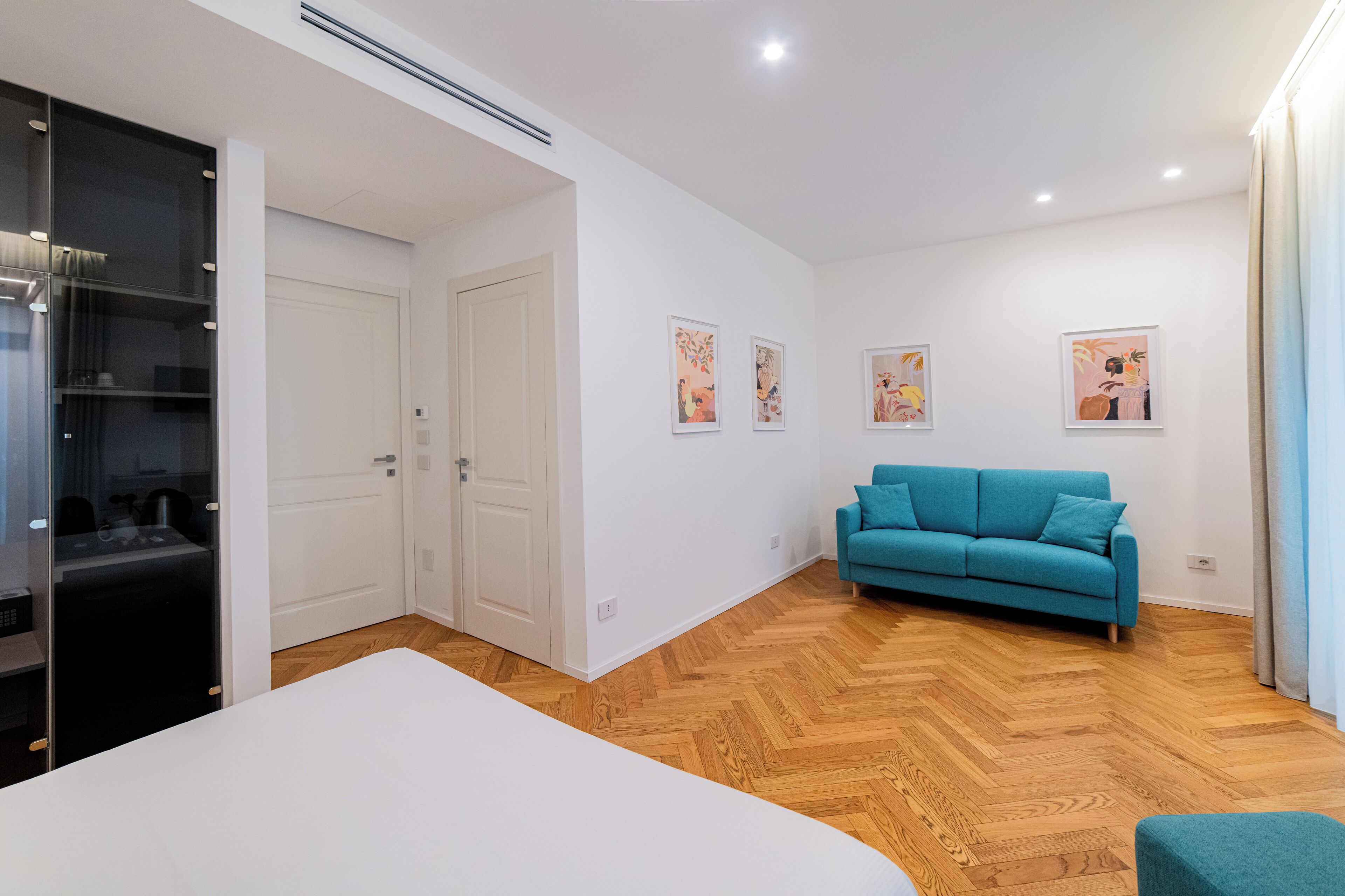 A modern bedroom with a large bed, a teal sofa, and a wardrobe.