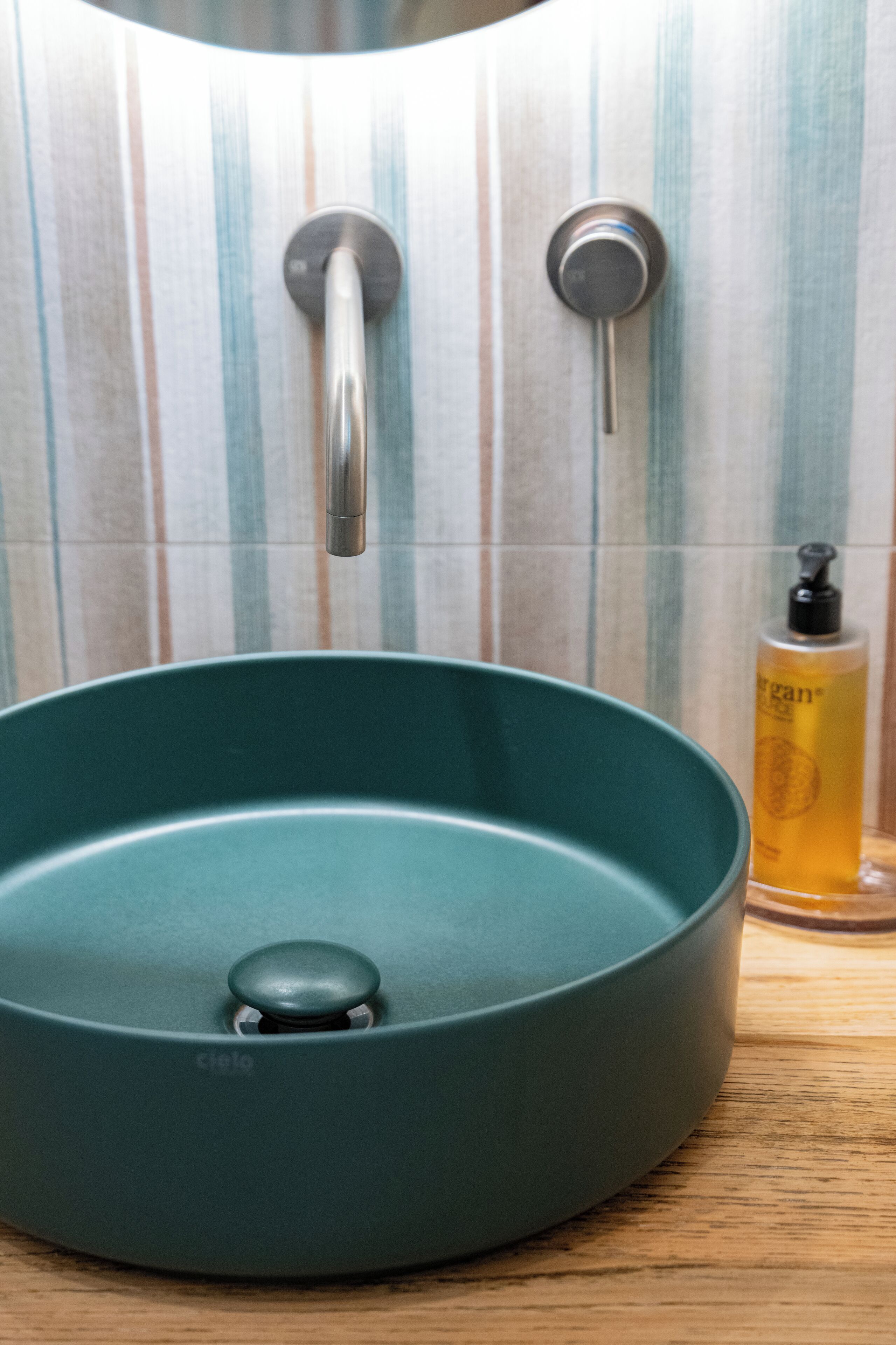 Ein Badezimmer mit einem türkisblauen Waschbecken, einem Wasserhahn und einer Seifenflasche auf der Ablagefläche.