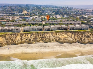 An aerial view of a coastal residential area with modern apartment buildings, a sandy beach, and a rocky cliff.