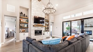 A spacious living room with a stone fireplace, a large gray sectional sofa, and a modern chandelier. - Escape to paradise in Texas Hill Country (Harker Heights)