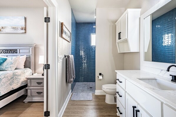 A bedroom with a bed, nightstands, and a dresser. There is a bathroom with a sink, mirror, and toilet. - Escape to paradise in Texas Hill Country (Harker Heights)