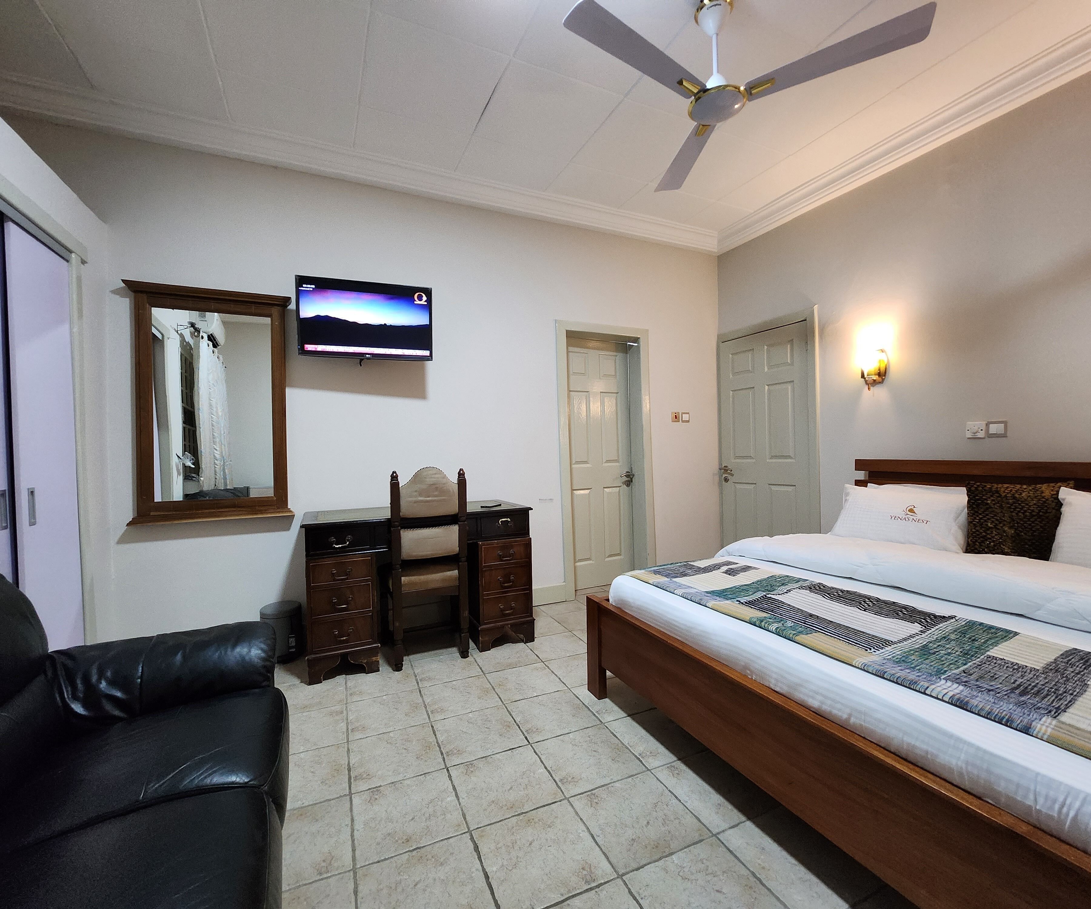 Un dormitorio con cama, escritorio, silla, televisor y ventilador de techo.