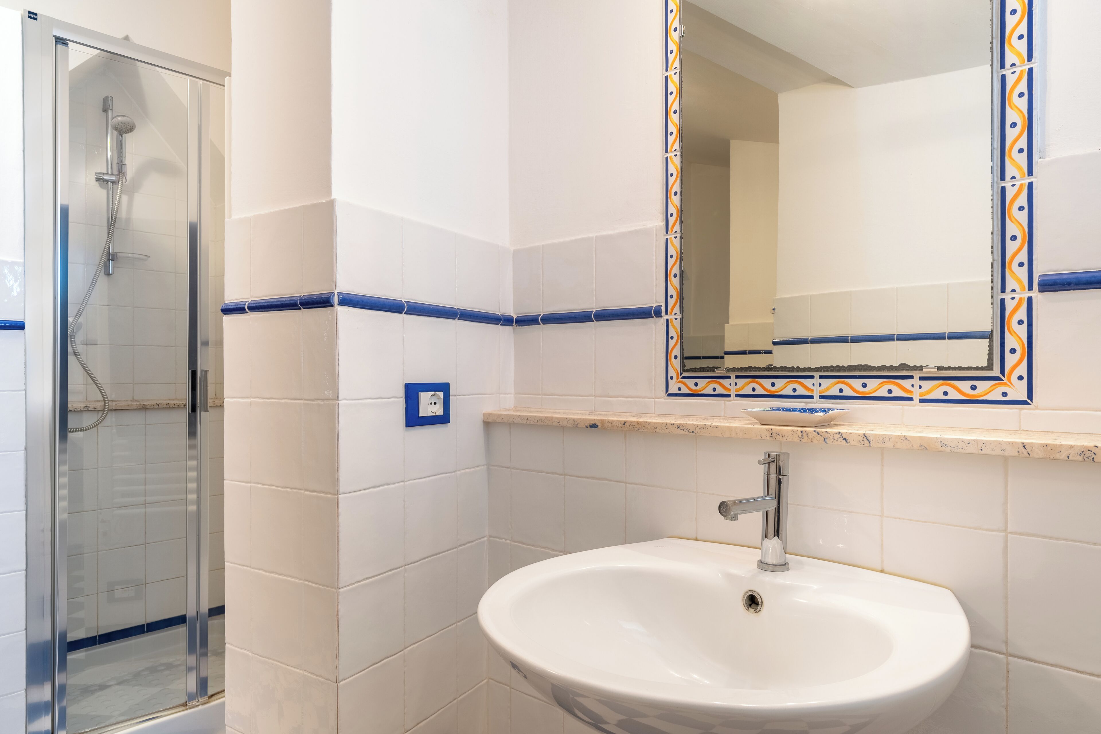 A bathroom with a glass-enclosed shower, a white sink, and a mirror with a decorative frame.