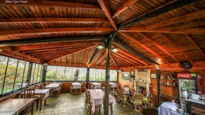 A rustic wooden dining area with tables and chairs, a Coca-Cola refrigerator, and a large window overlooking greenery. - Tartaruga Boutique Hotel & Bungalows (Sile)