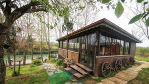 A wooden cabin with large windows, a stone pathway, and a view of a lake. - Tartaruga Boutique Hotel & Bungalows (Sile)