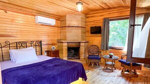 A wooden cabin room with a bed, a fireplace, a television, and a window with curtains. - Tartaruga Boutique Hotel & Bungalows (Sile)