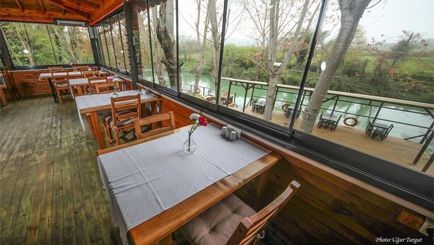 An indoor dining area with wooden tables and chairs, large windows offering a view of a lake and trees. - Tartaruga Boutique Hotel & Bungalows (Sile)