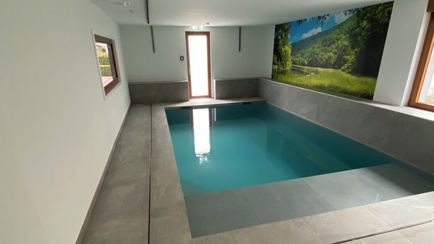 Ein Schwimmbecken mit gefliestem Boden und Wänden, ein gerahmtes Bild auf der linken Seite und ein großes Landschaftsgemälde auf der rechten Seite.