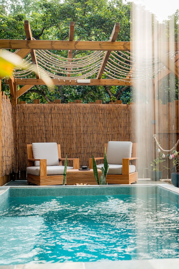 A pool area with two wooden chairs, a bamboo fence, and a hanging rope swing.