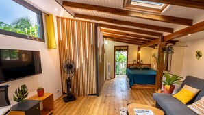 Ein modernes Wohnzimmer mit Fernseher, Holzboden, einer Couch und einem Bett mit Balkonblick.