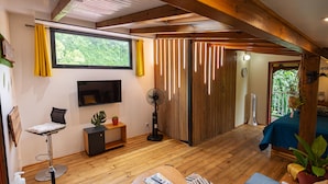 Ein modernes Wohnzimmer mit Holzboden, einem Flachbildfernseher, einem Essbereich mit Tisch und Stühlen sowie einer Couch.
