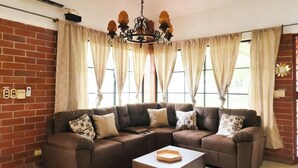 A living room with a brown sectional sofa, a wooden coffee table, and a chandelier.