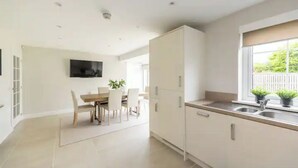 Cozinha moderna com armários brancos, área de refeições com mesa e cadeiras, e janela com plantas.