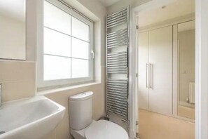 Un bagno con finestra, dotato di WC, lavandino e mobiletto a muro.