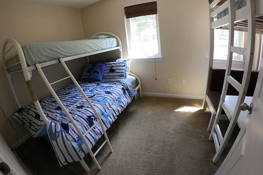 A bunk bed room with a window, carpeted floor, and a door with a handle.