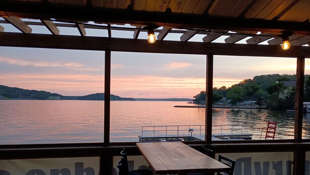 Une terrasse en bois avec une table et des chaises, donnant sur un lac au coucher du soleil.