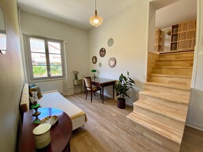 Une pièce chaleureuse avec un plancher en bois, une table à manger avec des chaises, un canapé, un petit bureau avec une lampe, une plante en pot et un escalier avec des rampes en bois.