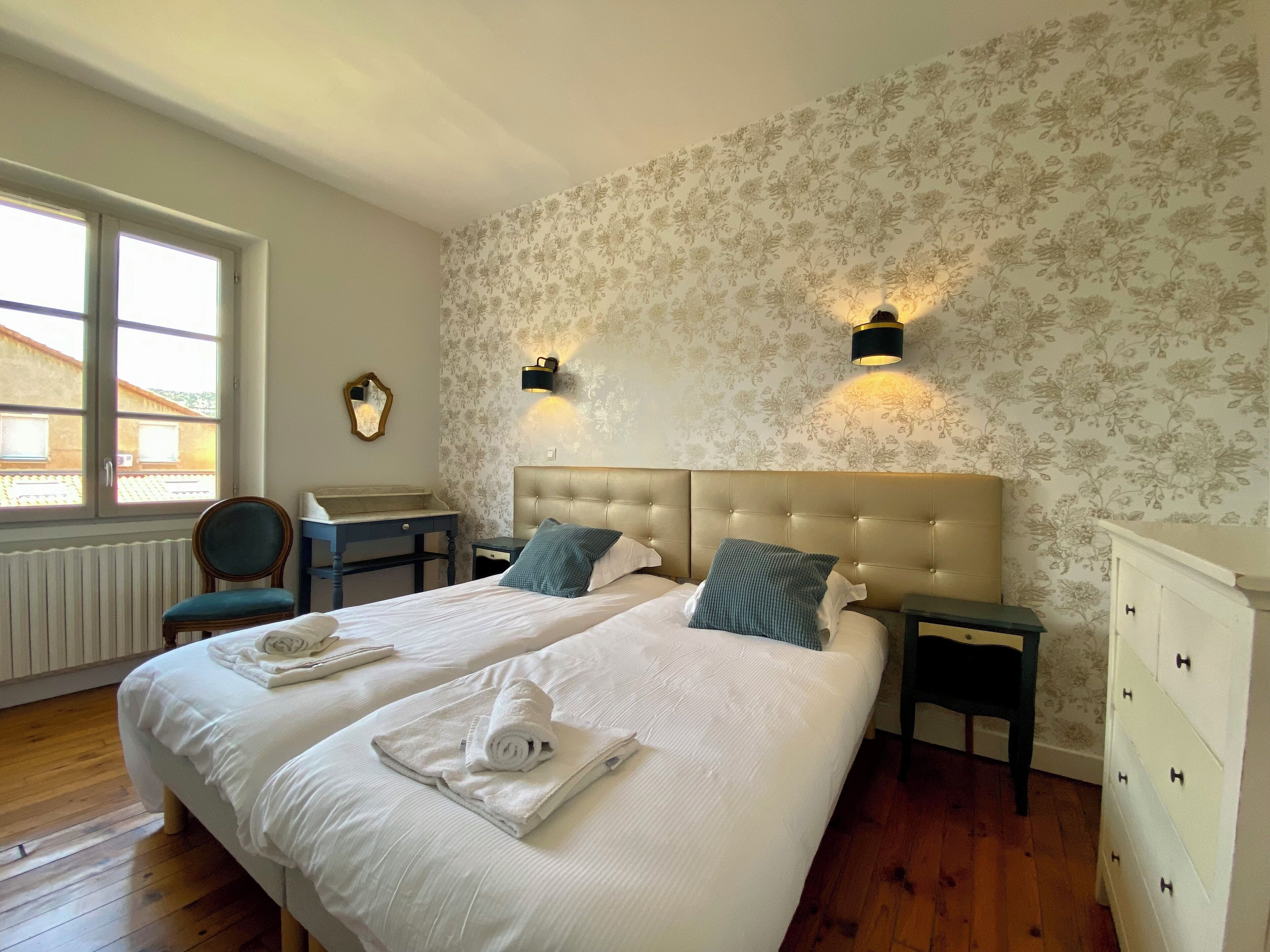 Une chambre d’hôtel avec un grand lit, deux tables de chevet, une chaise, une commode et une fenêtre donnant sur un beau paysage.