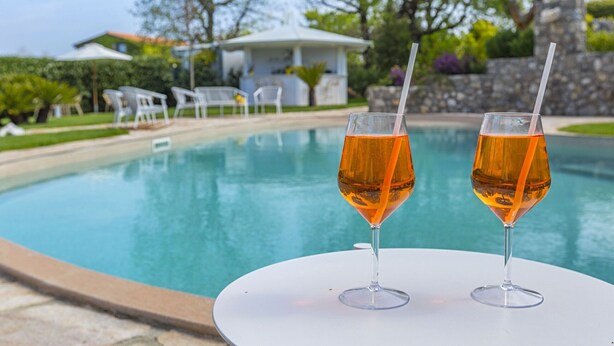 A poolside table with two glasses of amber liquid, a white umbrella, and a gazebo in the background. - Resort Ravella: Lord Executive room (Sant´Agata sui Due Golfi)