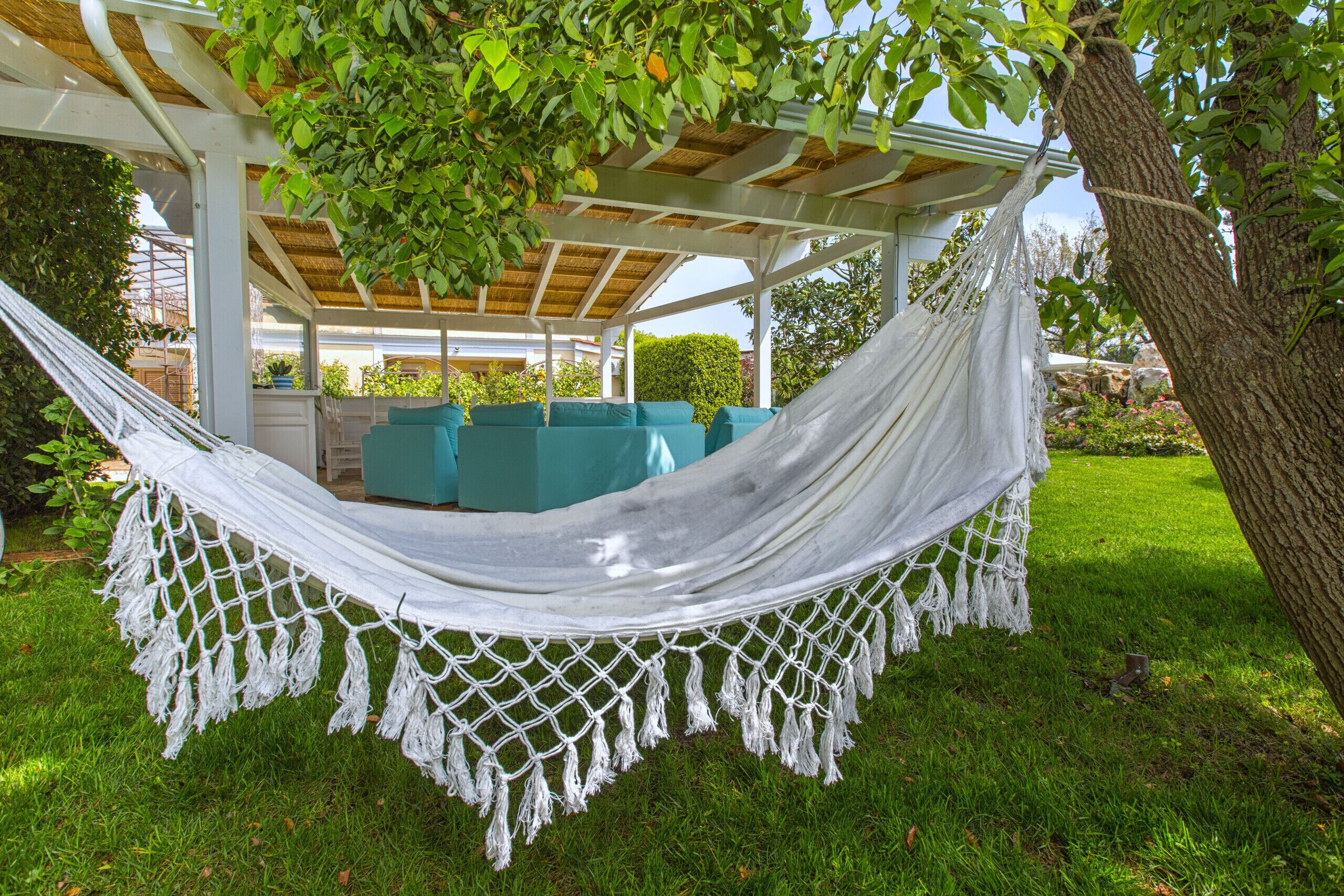 Eine Hängematte unter einer Pergola mit Blick auf einen Garten und Sitzgelegenheiten im Freien.