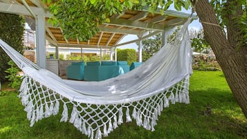 Eine Hängematte unter einer Pergola mit Blick auf einen Garten und Sitzgelegenheiten im Freien.