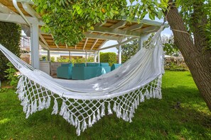 Un hamac sous une pergola, avec vue sur un jardin et un espace salon extérieur.