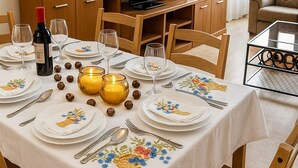 Zona pranzo con tavolo apparecchiato per quattro persone, televisore, pensili in legno e un divano sullo sfondo.