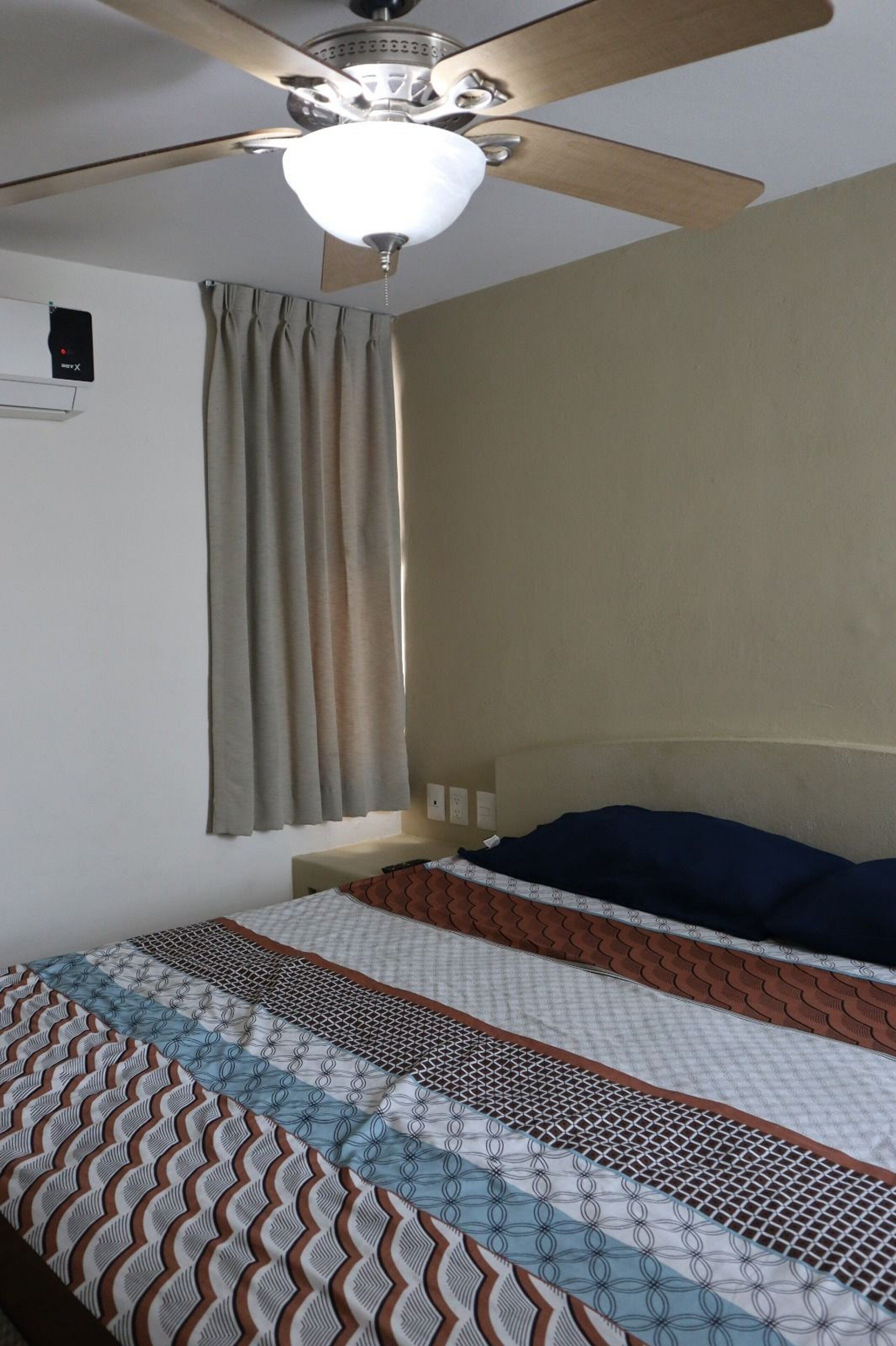 Quarto com cama, ventilador de teto e janela com cortinas.