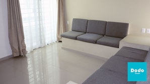 A modern living room with a grey sofa, a white coffee table, and a large window with sheer curtains. - Torre Altamar (Mazatlán)
