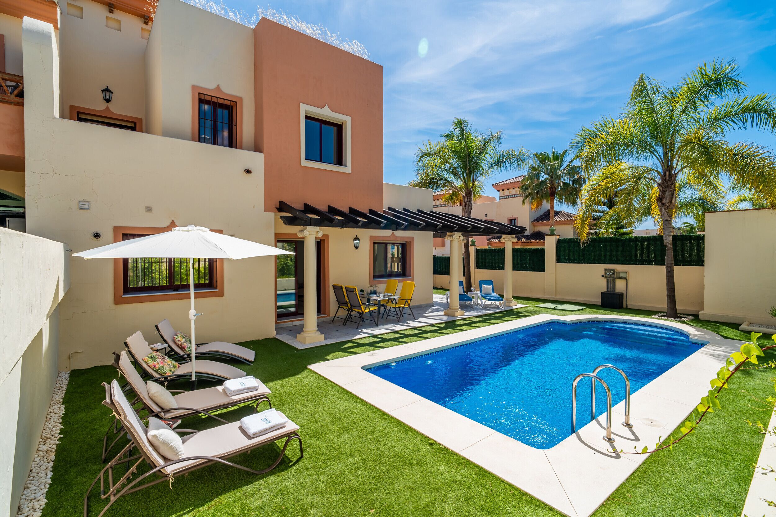 A swimming pool with lounge chairs and a pergola, surrounded by palm trees and a well-maintained lawn.