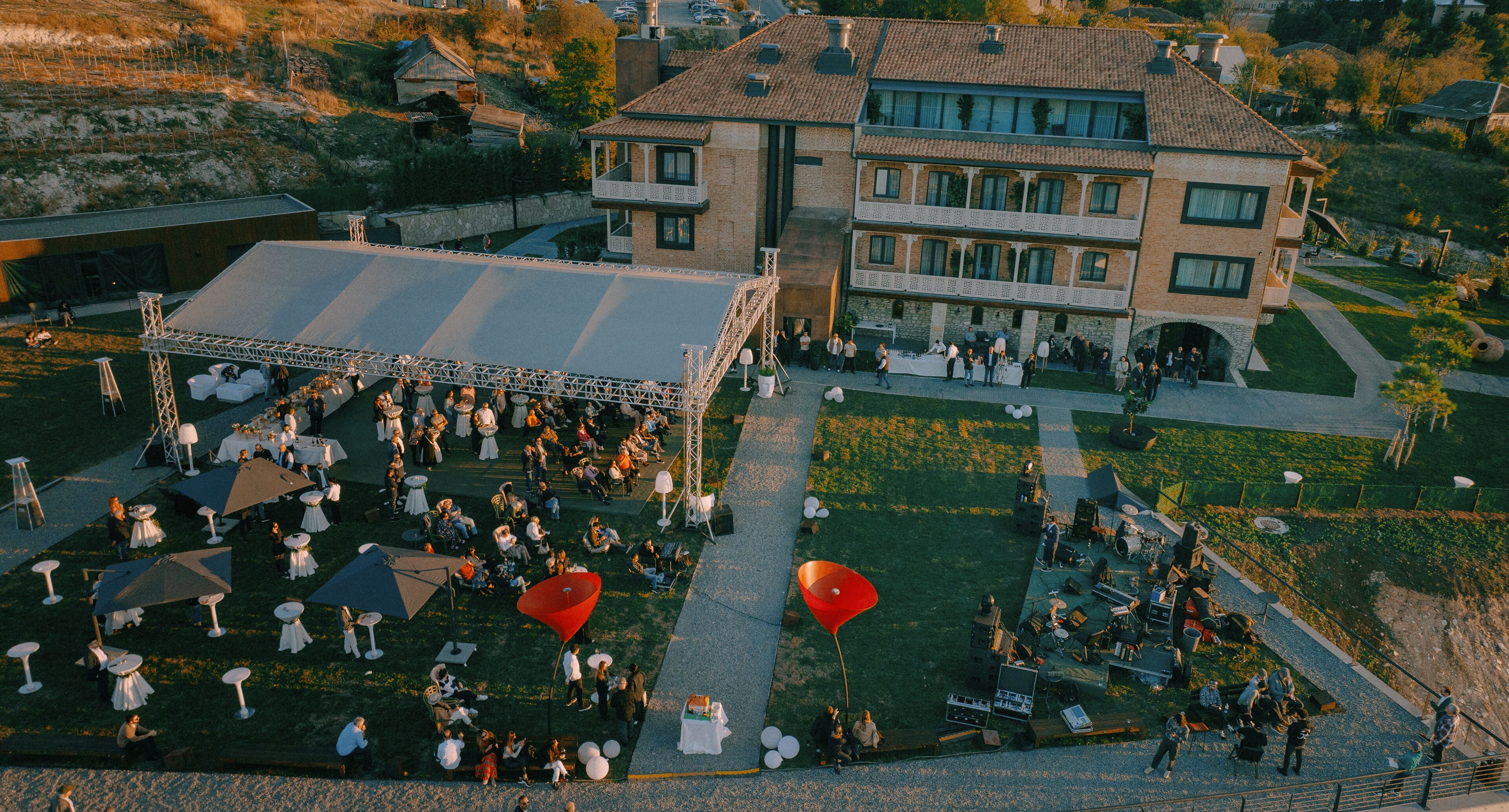 An outdoor event with tables and chairs arranged on a grassy area in front of a large building with multiple balconies.