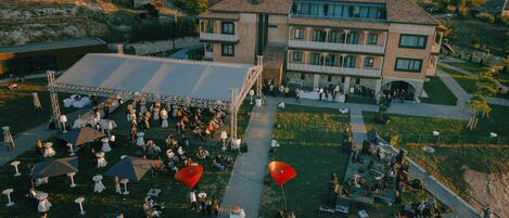 An outdoor event with tables and chairs arranged on a grassy area in front of a large building with multiple balconies.