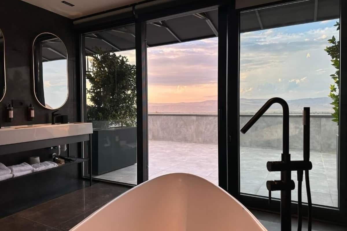 Ein modernes Badezimmer mit einer freistehenden Badewanne, einem großen Spiegel und Blick ins Freie.