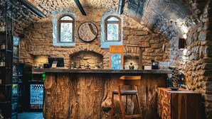 A rustic bar area with stone walls, wooden bar counter, and a large clock on the wall. - Chateau MephisKalaki (Kaspi)