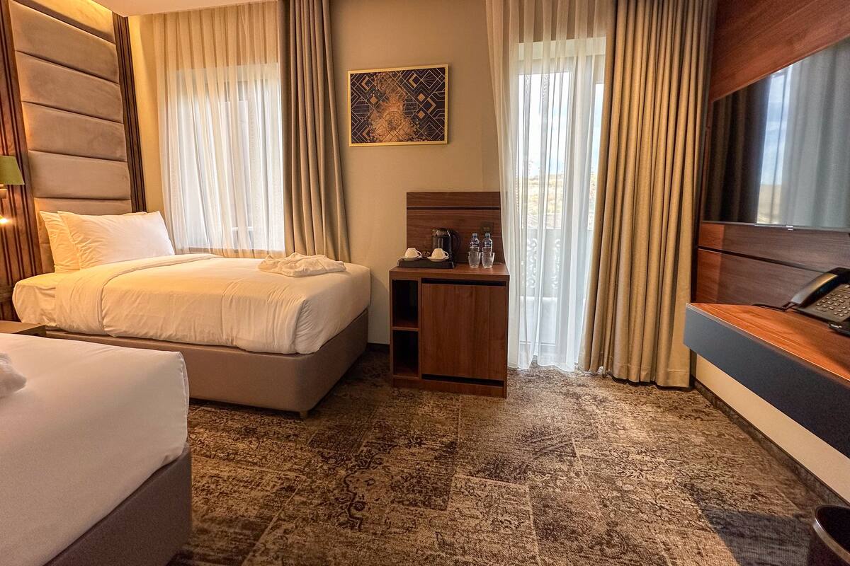Ein Hotelzimmer mit Bett, Schreibtisch, Stuhl, Fernseher und einem fensterbepflanzten Fenster.