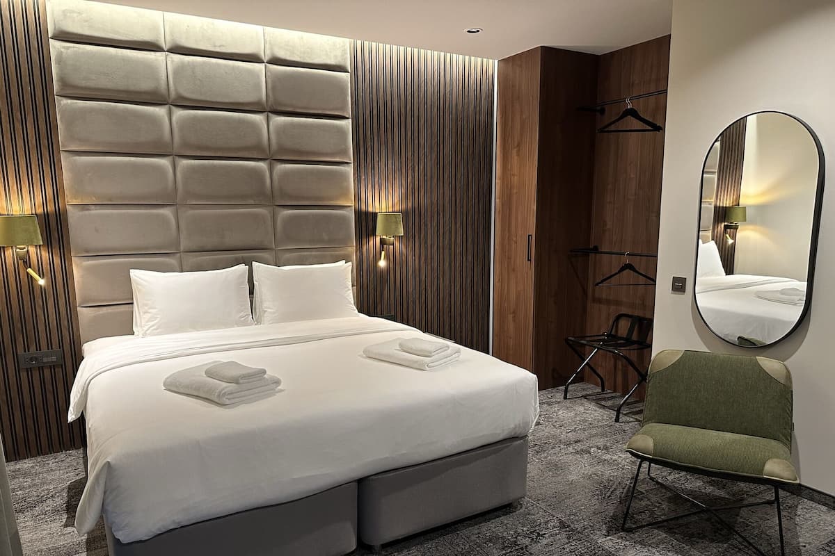 Ein modernes Hotelzimmer mit einem großen Bett, zwei Nachttischlampen, einem Spiegel, einem Sessel und einem Kleiderschrank.