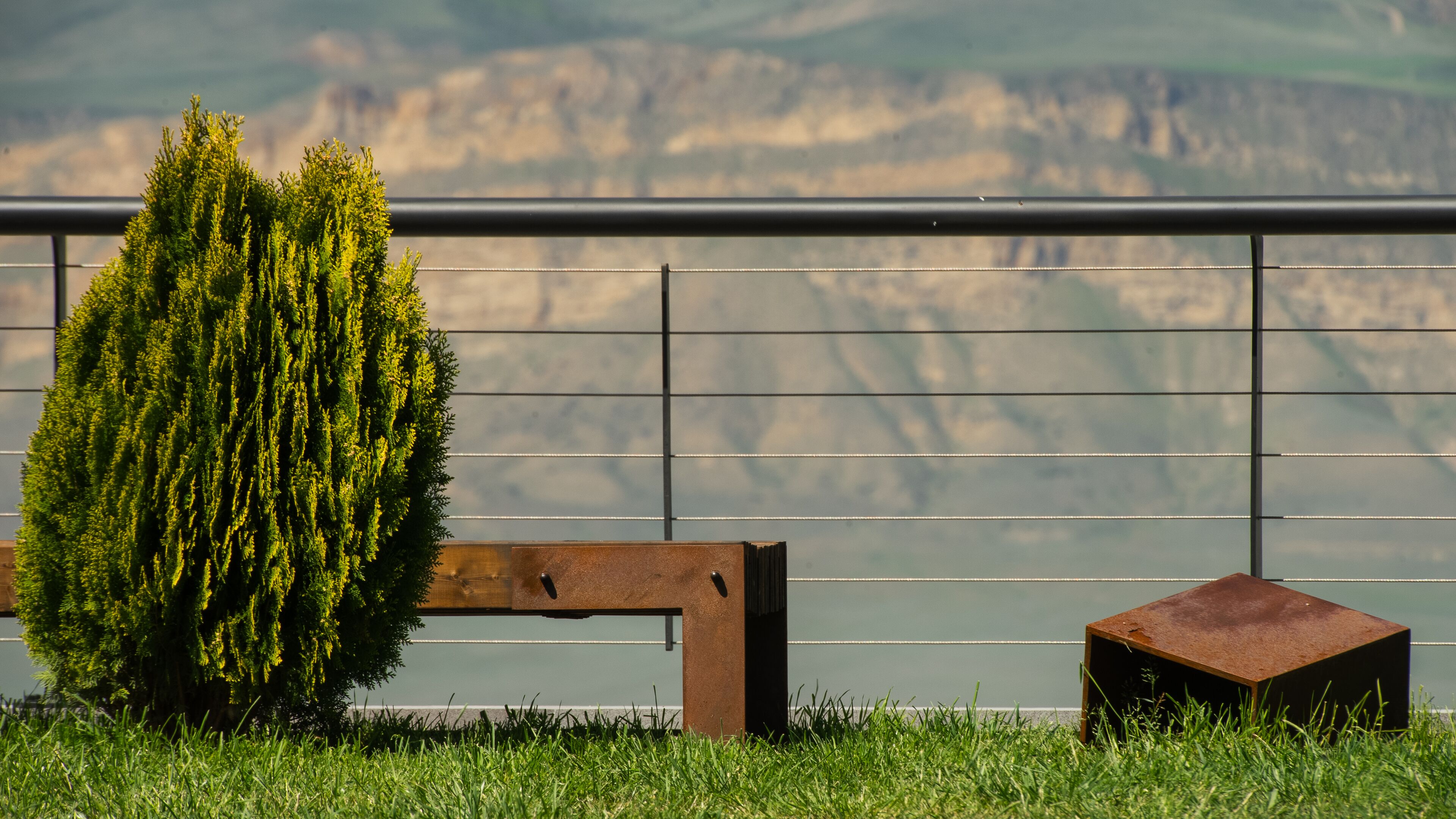 A bench and a small stool by a railing with a view of a mountainous landscape.