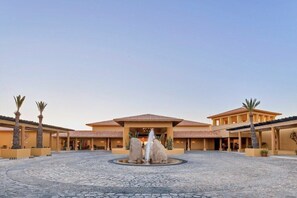 A hotel courtyard with a central fountain, palm trees, and a large building with a tiled roof. - Los Cabos | Couples All-Inclusive Retreat | Pool + Beach (Cabo del Sol)