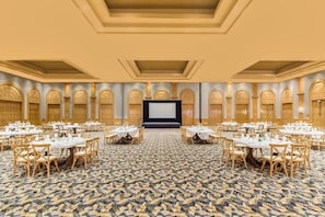 A banquet hall with round tables and chairs, a stage, and a patterned carpet.