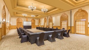 Un salón de conferencias con una larga mesa, sillas, candelabros y puertas de arco.