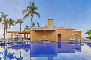 A pool area with lounge chairs and umbrellas, surrounded by palm trees.