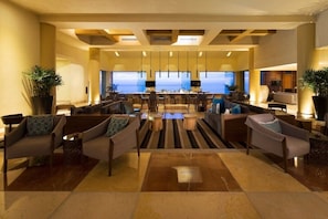 A spacious lobby with a bar area, seating arrangements, and a view of the ocean.