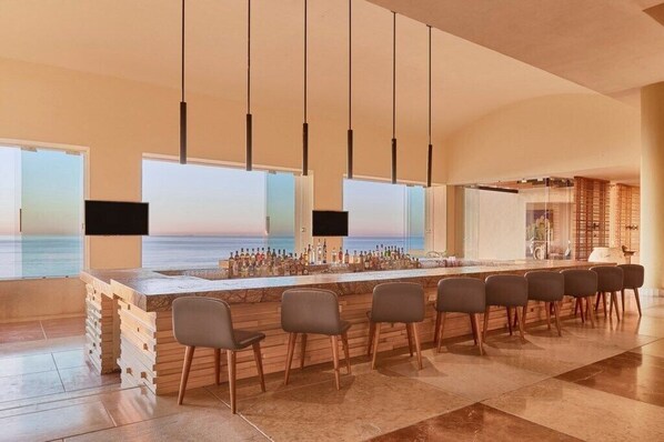 A bar area with a long counter, multiple chairs, and a view of the ocean.